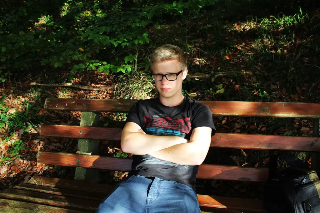 Jeune homme tout seul sur un banc les bras croisés. Signe possible d'une blessure de rejet.