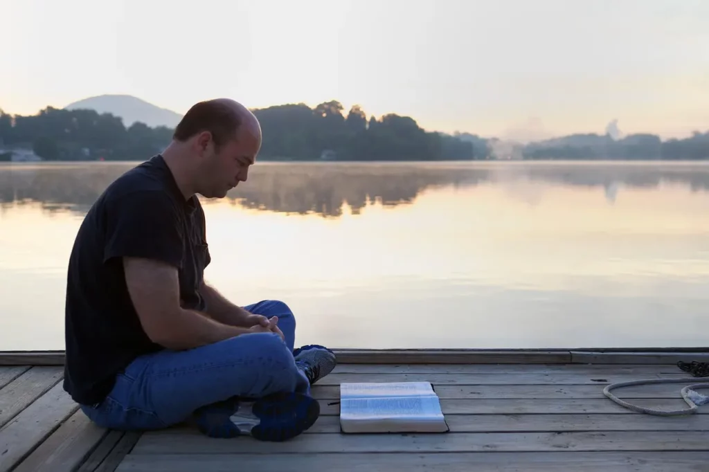 Homme sur un embarcadère assis au bord de l'eau en train de lire le soir. Cette image illustre l'année personnelle 7. Calculer et comprendre les années personnelles en numérologie.