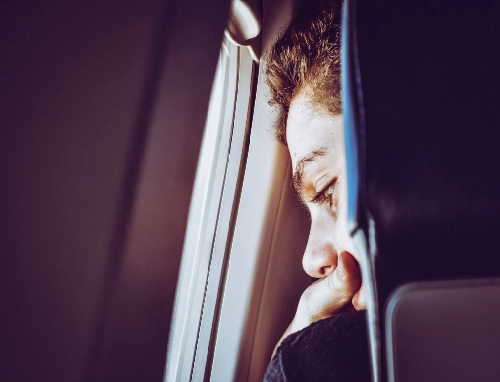 Jeune homme qui lance un regard inquiet à travers le hublot d'un avion. Peur de l'avion, comment l'accompagner avec l'hypnose ?